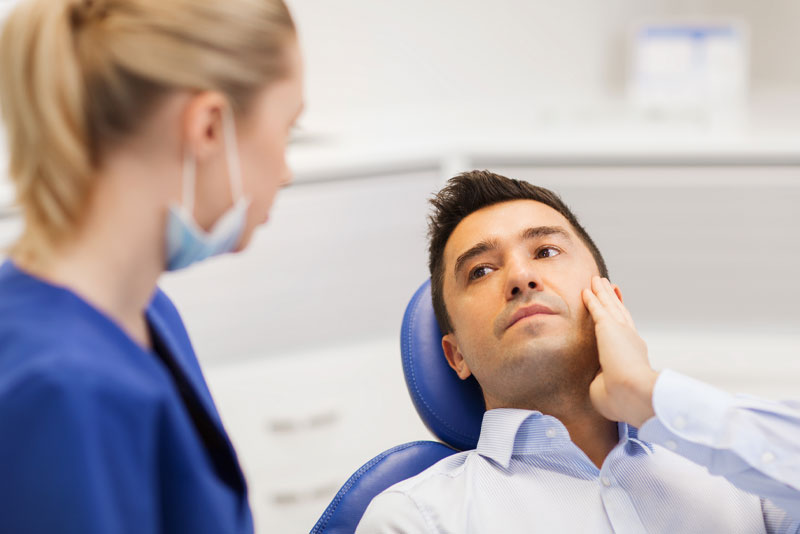 image of a dentist telling her patient he needs a root canal treatment as he touches the cheek where his tooth pain is.